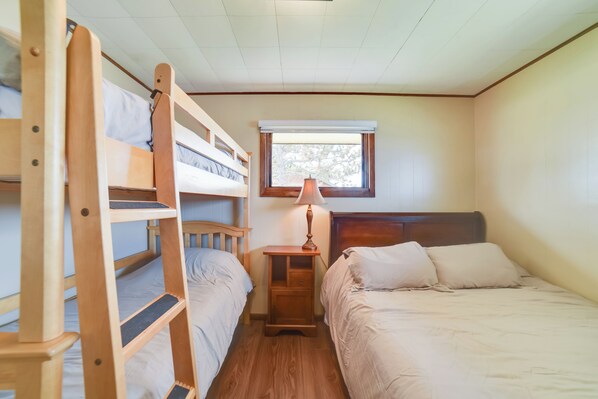 A dormitory room with bunk beds, a nightstand with a lamp, and a window with a view of trees. - BBQ Ready: Lakefront Retreat in Watertown (Watertown)