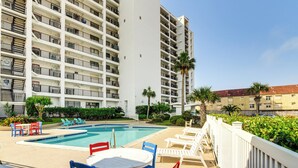 A hotel pool area with a large pool, lounge chairs, and a white fence.
