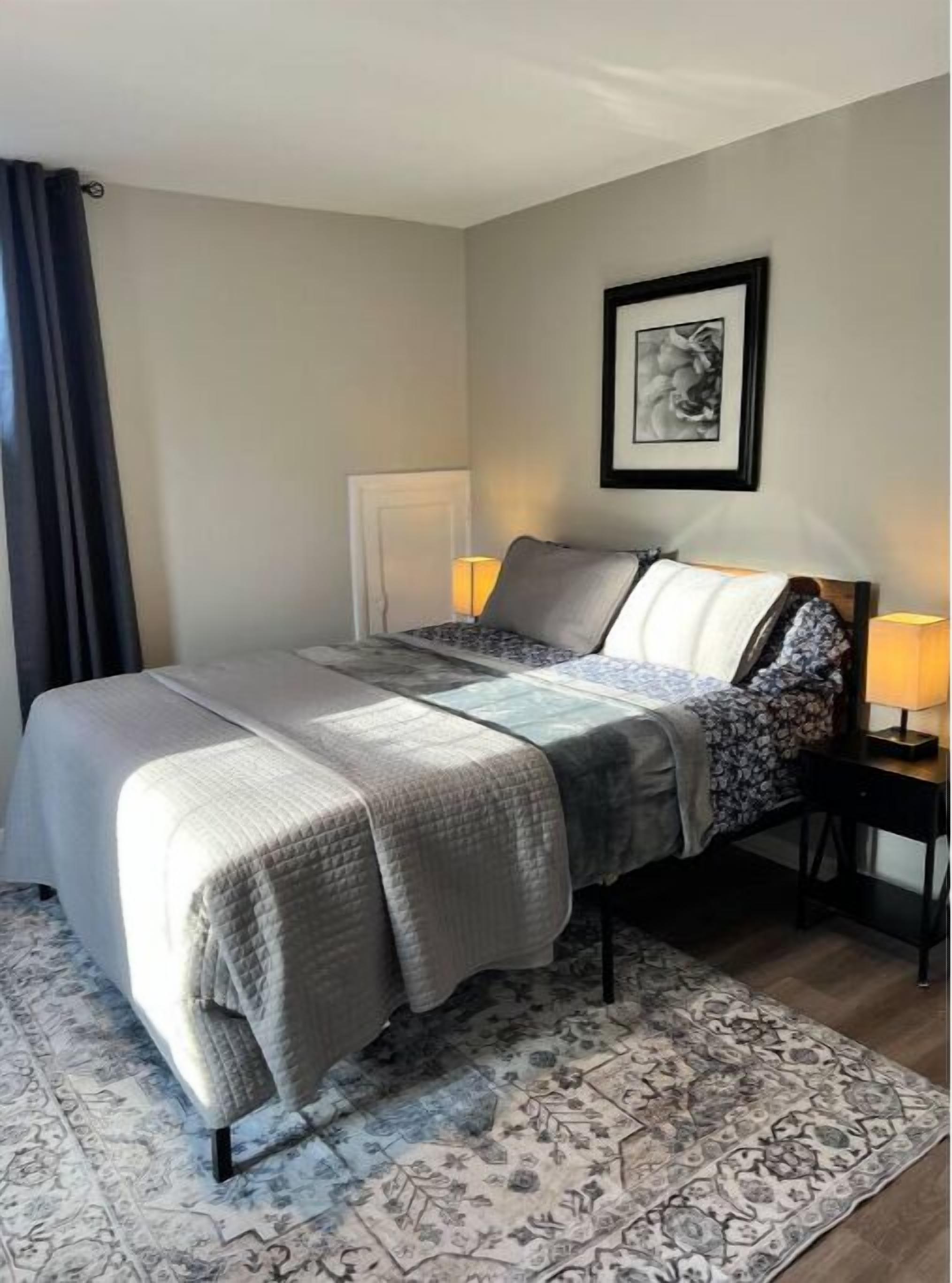 A neatly made bed with a patterned bedspread, a bedside table with a lamp, and a framed picture on the wall.