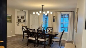 A dining area with a wooden table and chairs, a chandelier, and a view of the outside through a window with curtains. - Spacious 3bdr 2ba - walk to Breweries & Downtown (Burlington)