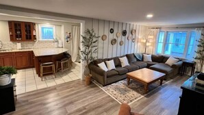 A modern living room with a sectional sofa, a coffee table, and a dining area with a kitchen in the background. - Spacious 3bdr 2ba - walk to Breweries & Downtown (Burlington)