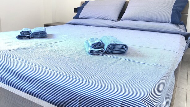 Ein ordentlich bezogenes Bett mit blau gestreifter Bettwäsche und Kissen, eine Wand mit einer Steckdose und ein kleines dekoratives Element an der Wand.