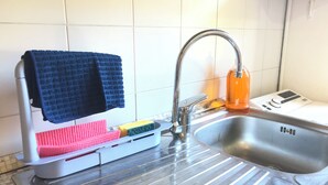 Eine Küche mit Spüle aus Edelstahl, einer Flasche Geschirrspülmittel und einem Geschirrgestell mit Schwämmen und Handtuch.