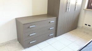 Ein modernes, minimalistisches Zimmer mit einem grauen Kleiderschrank, der mehrere Schubladen und einen hohen Schrank mit zwei Türen bietet.