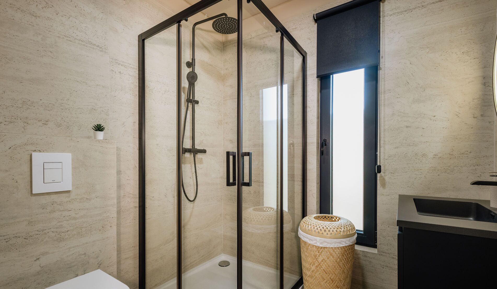 A modern bathroom with a glass-enclosed shower, a small potted plant, and a large window.