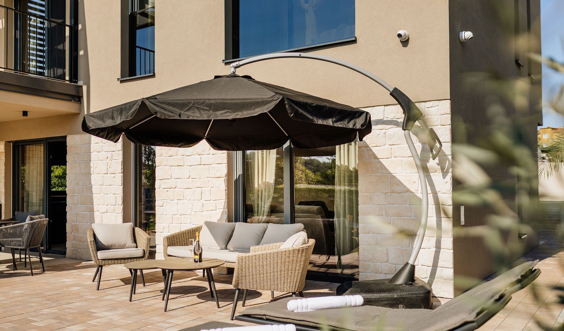 An outdoor seating area with wicker furniture, a large umbrella, and a glass-enclosed space.