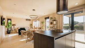 A modern kitchen with a central island, a dining area with a round table, and a large window offering a view of the outdoors.