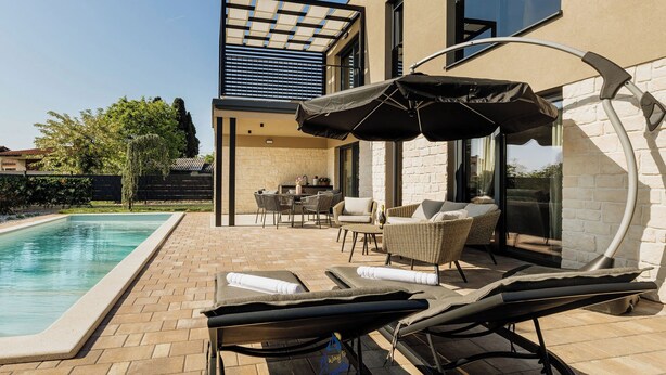 A modern outdoor pool area with lounge chairs and umbrellas, a dining set, and a stone wall.