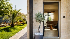 A modern building with a stone facade, a well-maintained garden with palm trees, and a visible interior with a sofa and a coffee table.