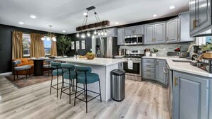 A modern kitchen with grey cabinets, stainless steel appliances, and a central island with bar stools. - Dream House | HotTub+Game Room | 11mi to Camelback (Pocono Summit)
