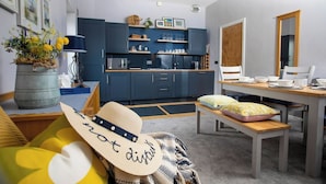 Een gezellige woonkamer met een bank, een eettafel en een keukenhoek met blauwe kastjes en een houten aanrechtblad.