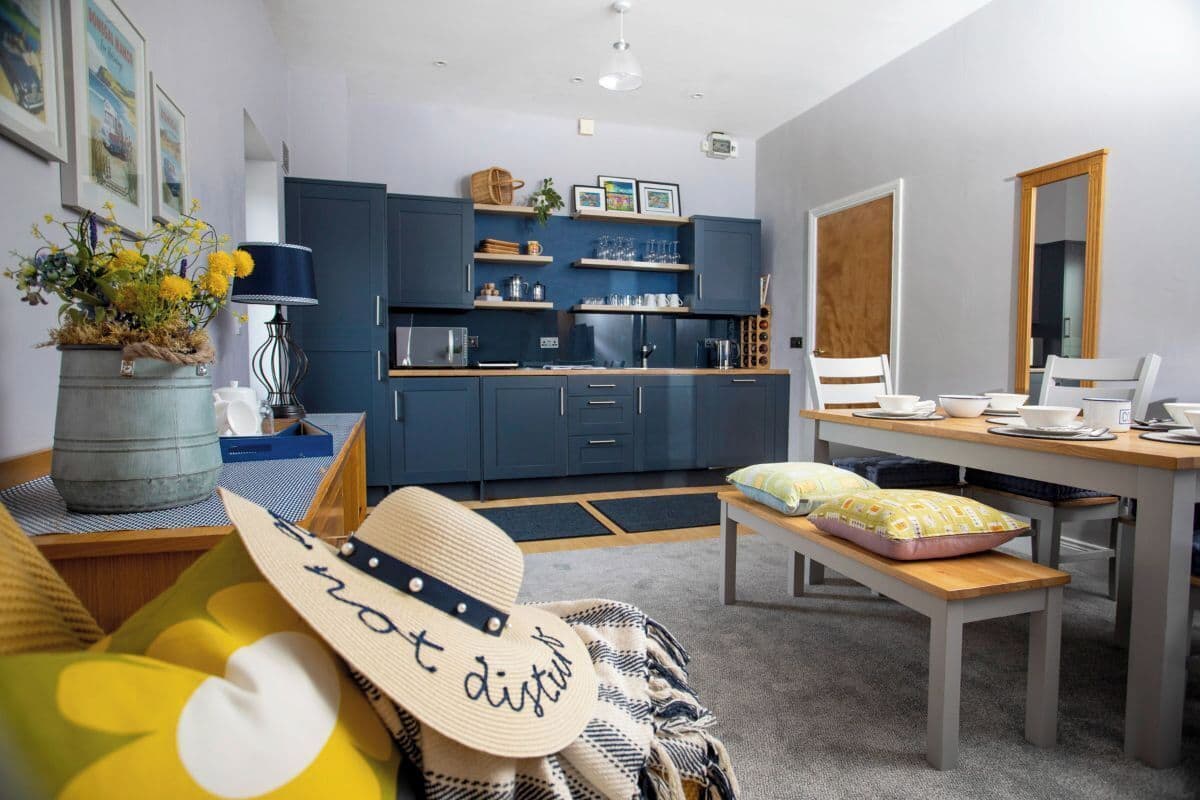 A cozy living room with a sofa, a dining table, and a kitchen area with blue cabinets and a wooden countertop.