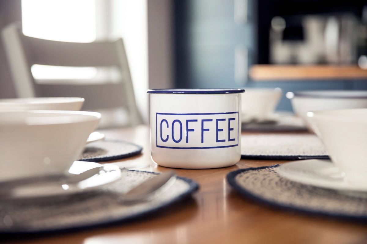 Una taza de café con la palabra 'COFFEE' escrita, sobre una mesa con una silla al fondo.