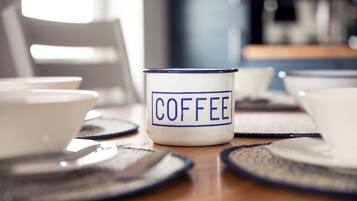 Una taza de café con la palabra 'COFFEE' escrita, sobre una mesa con una silla al fondo.