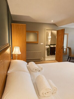 Ein Hotelzimmer mit Bett, Lampe, Spiegel, einer Tür zu einem Badezimmer und einem Sessel.