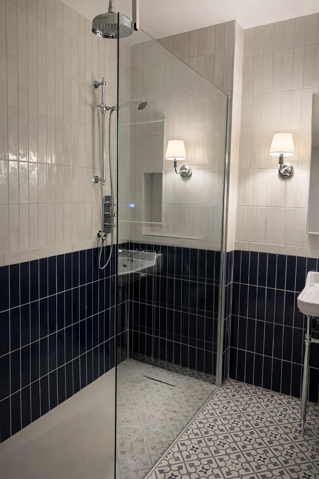 A bathroom with a glass shower enclosure, a sink, and two wall-mounted lights.