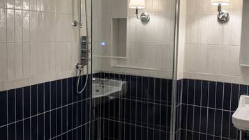 A bathroom with a glass shower enclosure, a sink, and two wall-mounted lights.