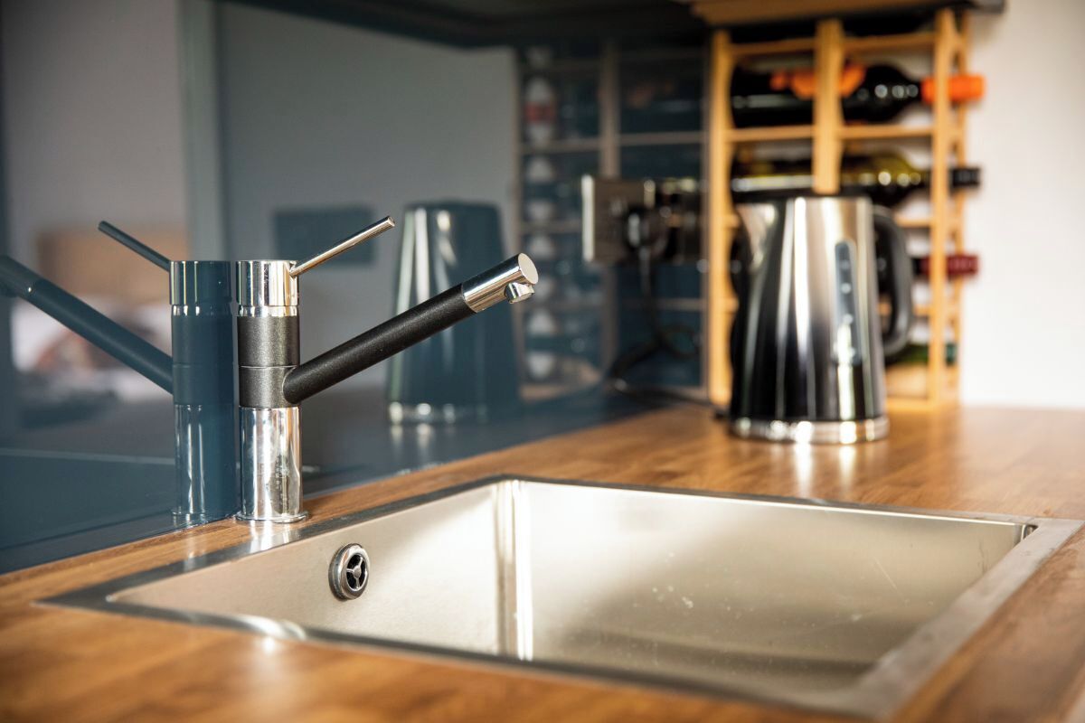A kitchen with a stainless steel sink, a modern faucet, and a kettle on the counter.