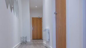 Un pasillo con suelo de madera, paredes blancas y una puerta de madera al final.