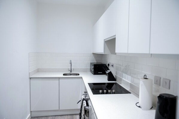 A modern kitchen with white cabinetry, a black stove, and a microwave. - The Hive - 2 Bed Luxury Apartment near Co-op Live (Manchester)