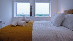 Habitación de hotel con cama, ventana con vista a la ciudad y pared de acento amarilla.