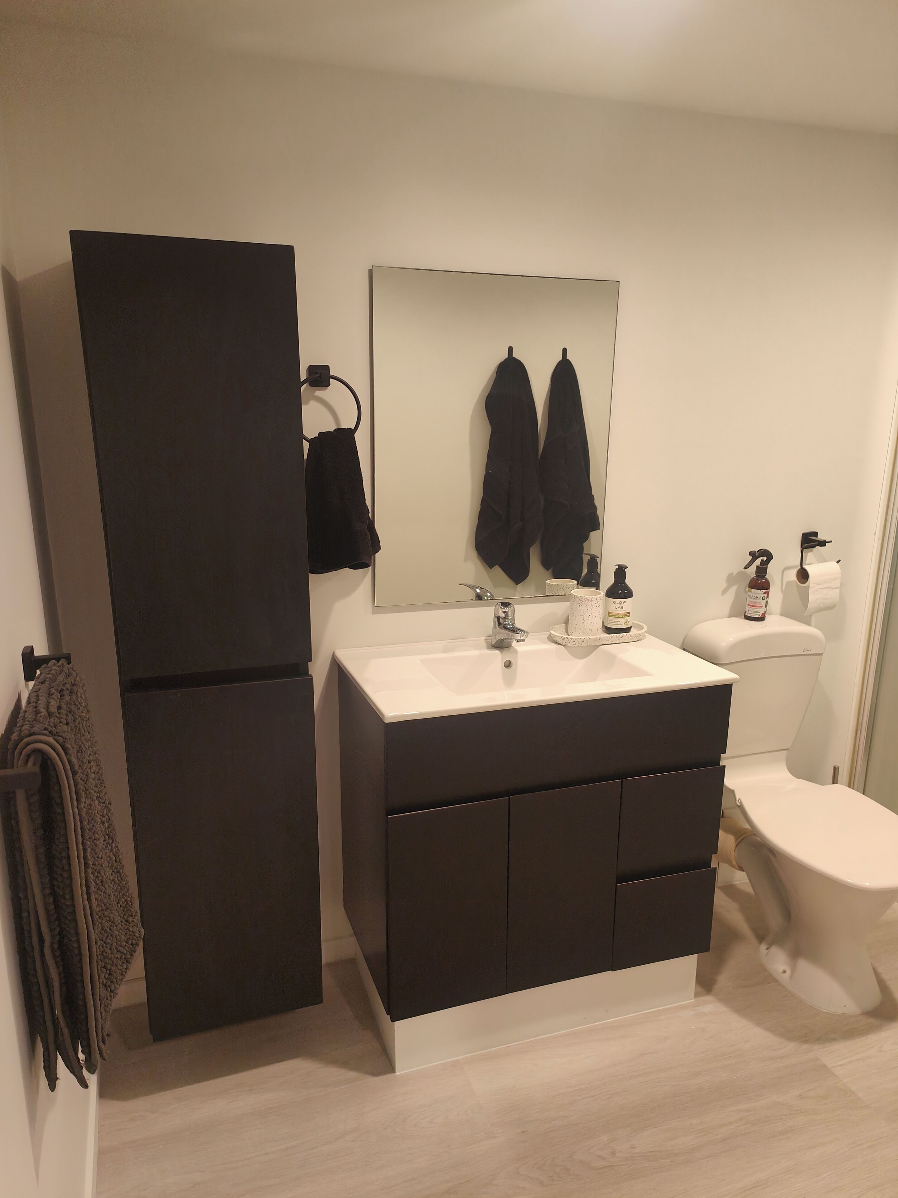 Et moderne badeværelse med et mørkt skab, en hvid vask og et toilet.