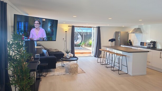 A modern living room with a flat-screen TV, a sofa, a coffee table, and a dining area. - Beautiful Studio w/Parking | Near CBD & Port Hills (Christchurch)