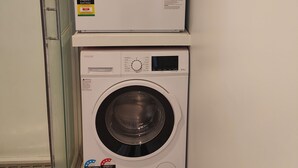 Two stacked front-loading washing machines in a laundry room with a glass door and a white wall. - Beautiful Studio w/Parking | Near CBD & Port Hills (Christchurch)