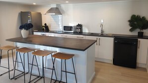 A modern kitchen with a central island, bar stools, a dishwasher, and a sink. - Beautiful Studio w/Parking | Near CBD & Port Hills (Christchurch)