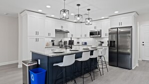 Una cocina moderna con armarios blancos, un refrigerador de acero inoxidable y una encimera de granito.