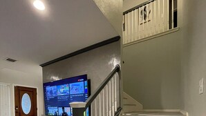 A modern interior with a staircase, a wooden cabinet, and a flat-screen TV mounted on the wall. - Centrally Located 4-Bed Getaway with 2.5 Baths (San Antonio)