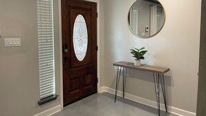 A hallway with a wooden door, a white-framed mirror, and a small table with a plant. - Centrally Located 4-Bed Getaway with 2.5 Baths (San Antonio)