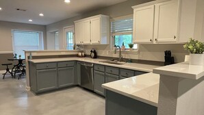 A modern kitchen with grey cabinets, a white countertop, and a built-in dishwasher. - Centrally Located 4-Bed Getaway with 2.5 Baths (San Antonio)