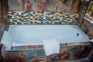 A rectangular bathtub with a mosaic tile backsplash and stone-patterned walls.