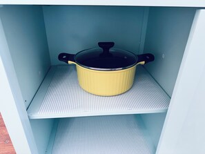 Una olla amarilla con tapa negra sobre un estante blanco dentro de un armario.