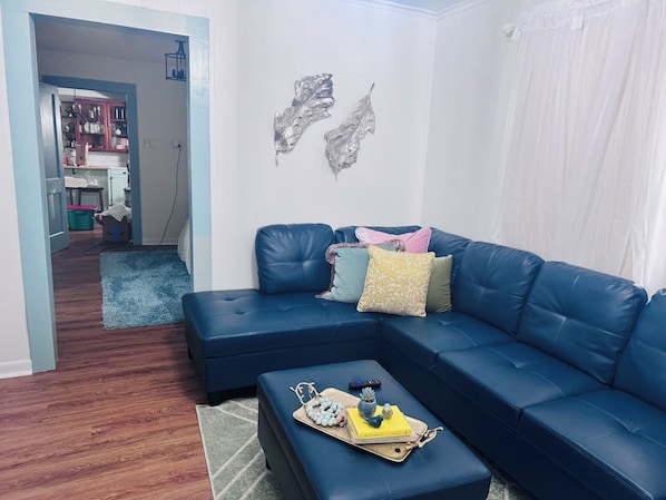 Un salón con un sofá azul, un pequeño reposapiés y almohadones decorativos.