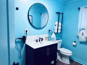 A bathroom with a white sink, black faucets, a round mirror, a toilet, and a towel rack with white towels.
