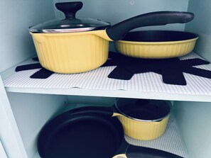 A kitchen shelf with cookware, including a yellow pot and pan set.
