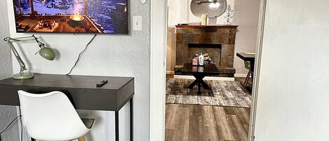 A modern living room with a TV mounted on the wall, a desk with a chair, a fireplace, and a ceiling fan.