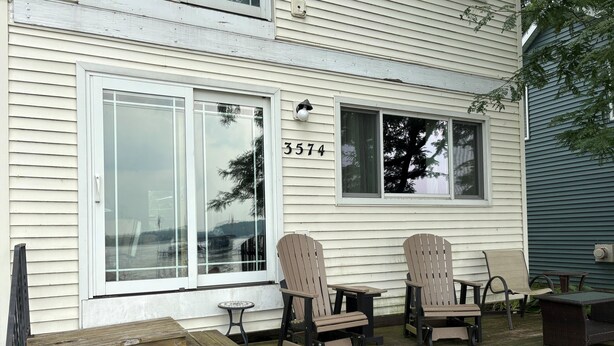 A house with a porch, two Adirondack chairs, a small round table, and a wooden bench.