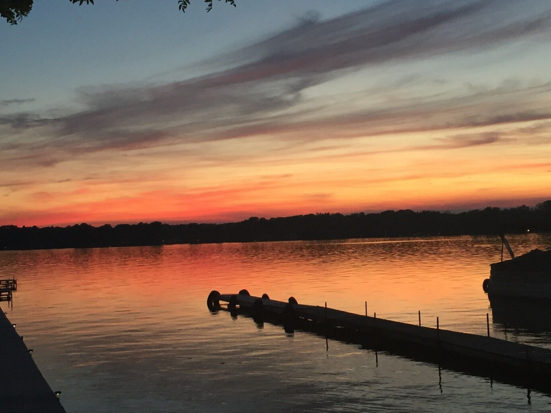 A calm lake at sunset with a dock and a boat.