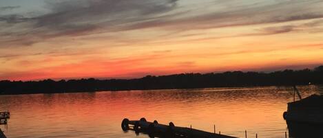 A calm lake at sunset with a dock and a boat.