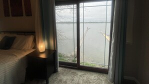 A bedroom with a bed, a nightstand, and a view of a lake through a sliding glass door.