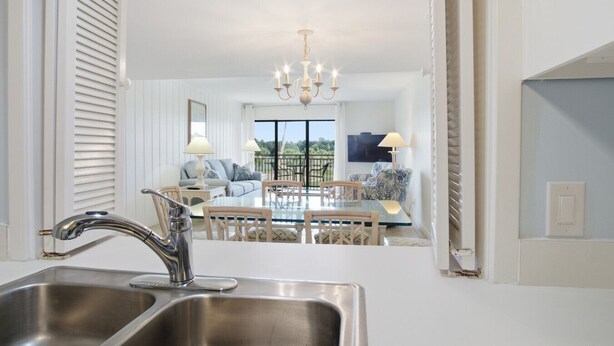 A modern kitchen with a stainless steel sink and a dining area with a glass table and chairs. - Fairway Haven – Minutes to Beach & Harbour Town (Hilton Head Island)