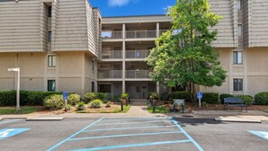 A multi-story parking lot with blue handicapped parking spaces, a building with a balcony, and a tree in the foreground. - Fairway Haven – Minutes to Beach & Harbour Town (Hilton Head Island)