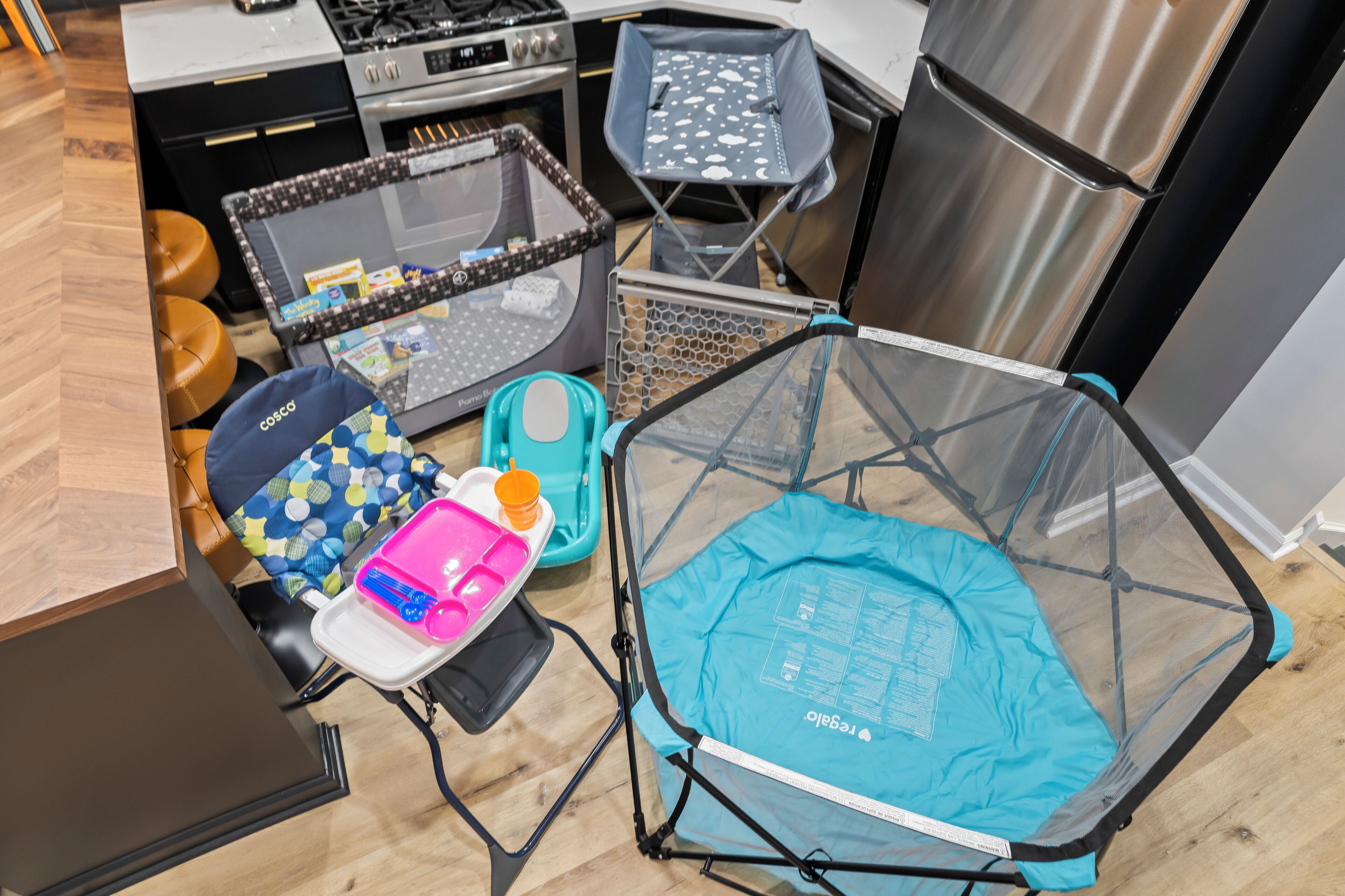 Et køkken med en rejse-babyseng, babystol og opbevaringskasser.
