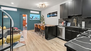 Una cocina moderna con encimera negra, electrodomésticos de acero inoxidable y una zona de comedor con sillas de madera y una pequeña mesa.