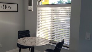 Ein Essbereich mit einem Marmortisch und zwei Stühlen, einem gerahmten Schild an der Wand und einem Fenster mit Jalousien.