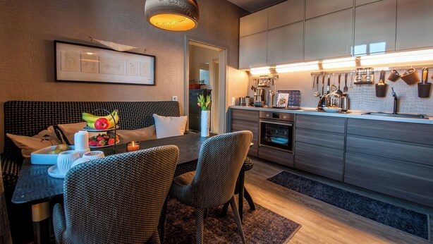 A modern kitchen with grey cabinets, a dining area with wicker chairs, and a hanging light fixture.