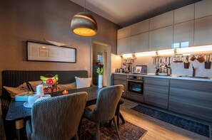 Een moderne keuken met grijze kastjes, een eethoek met rieten stoelen, en een hanglamp.